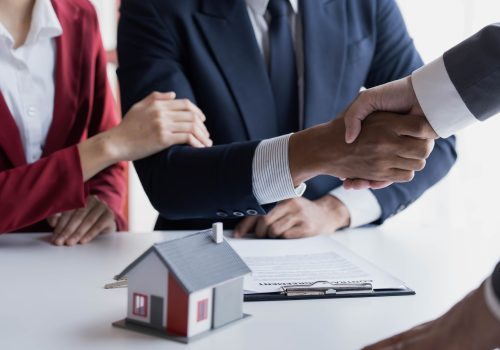 Happy couple first time home owners handshaking realtor insurer landlord bank worker at meeting